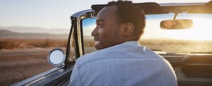 Rear View Of Man On Road Trip Driving Convertible Toward Sunset