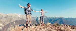 Man and woman holding hands on top of a mountain, confident in their ability to pay abroad.